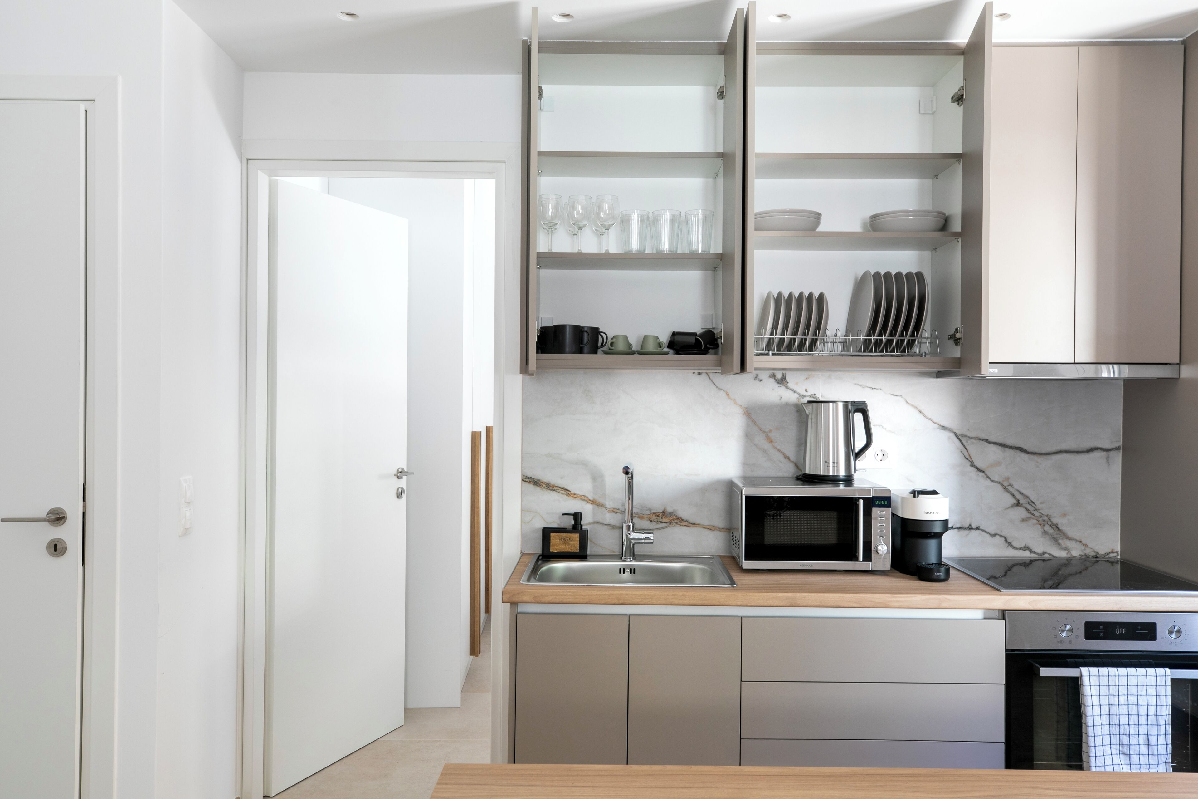 A modern kitchen with a wooden countertop, stainless steel appliances, and open shelving with dishes and glasses.