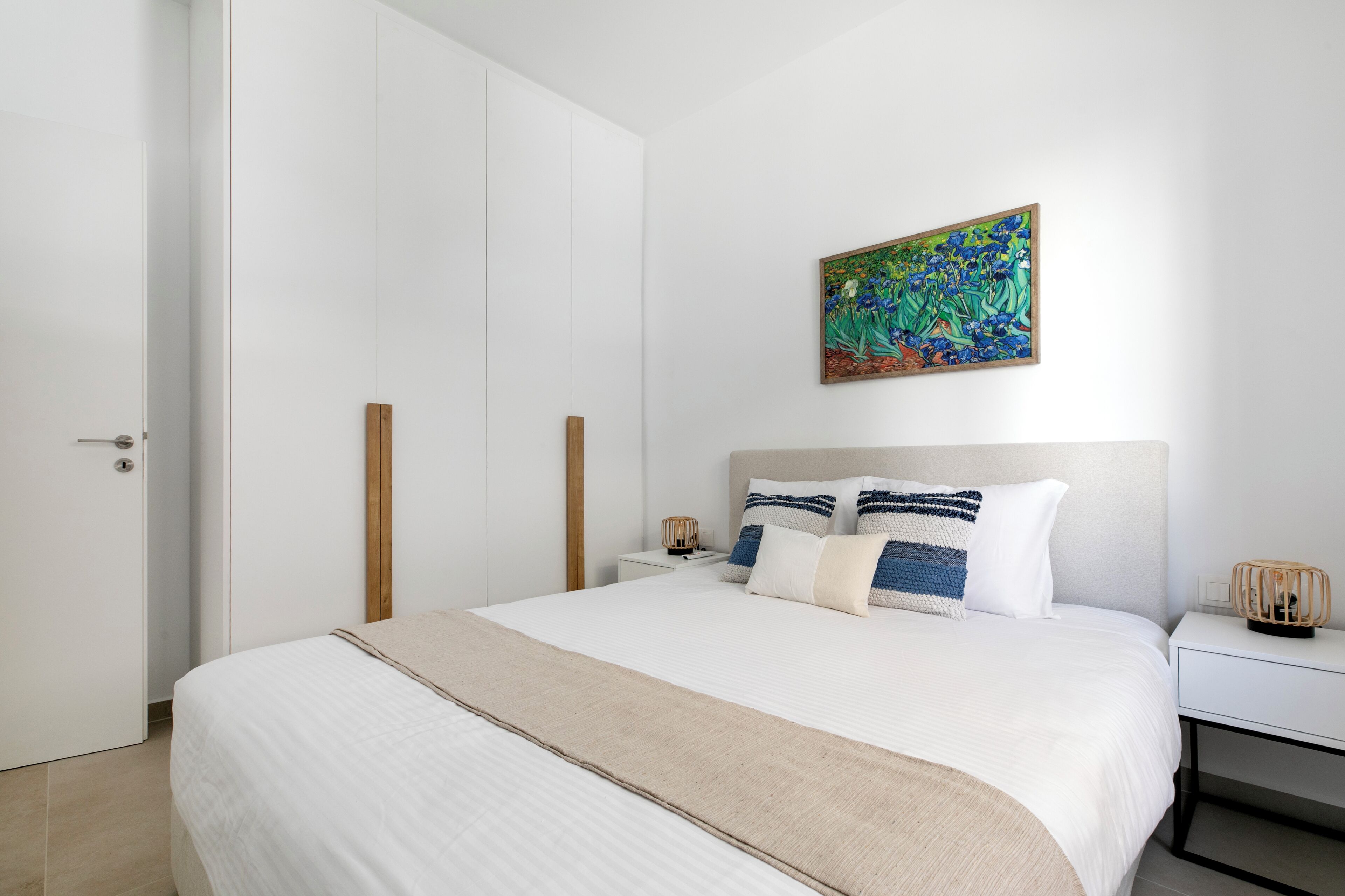 Ein aufgeräumtes Schlafzimmer mit einem großen Bett, einem Nachttisch mit Lampe und einem Wandbild.