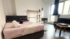 A bedroom with a bed, a wooden floor, a window with curtains, a small table, and a chair. - London Luxe Apartment - Spacious & Stylish (London)