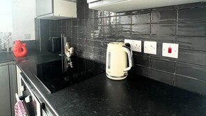 A modern kitchen with black countertops, a kettle, and a coffee maker. - London Luxe Apartment - Spacious & Stylish (London)