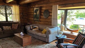 Acogedor interior de cabaña de madera con sofá, sillón y una mesita.