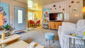 A modern living room with a sofa, ottoman, and a coffee table. There is a TV mounted on the wall and a dining area with chairs and a table. - Lustron of the Lakes: Retro MCM Gem in Tangletown (Minneapolis)