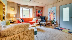 A cozy living room with a red sofa, a blue armchair, and a fluffy beige armchair. There is a painting of an astronaut on the wall, a lamp, and a small table with a plant. - Lustron of the Lakes: Retro MCM Gem in Tangletown (Minneapolis)