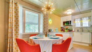 A dining area with a round table set for four, surrounded by orange chairs. A kitchen is visible in the background with white cabinets and a microwave. - Lustron of the Lakes: Retro MCM Gem in Tangletown (Minneapolis)