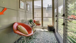 A room with a patterned floor, two red chairs, a small table with a plant, and a window with a view of greenery and buildings. - Lustron of the Lakes: Retro MCM Gem in Tangletown (Minneapolis)