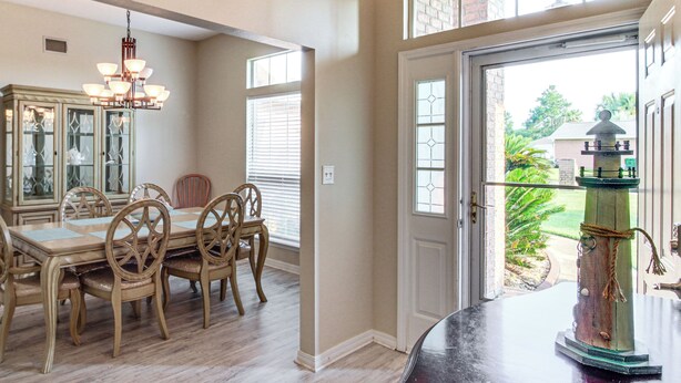 A dining area with a wooden table and chairs, a chandelier, and a view through a door to the outside. - Outdoor Oasis: Group Getaway in Pensacola! (Pensacola)
