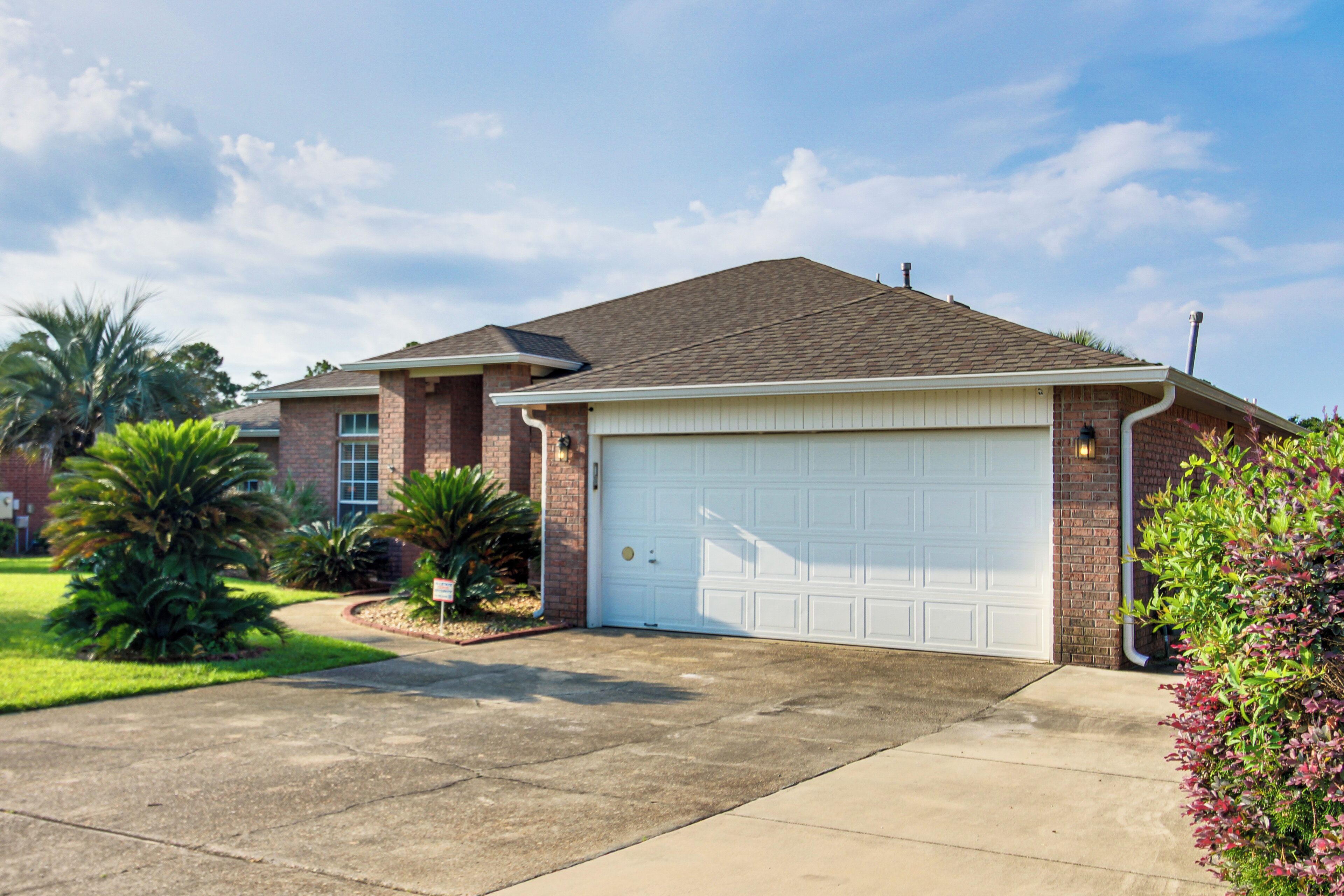 A residential house with a garage, brick exterior, and a well-maintained lawn with palm trees.