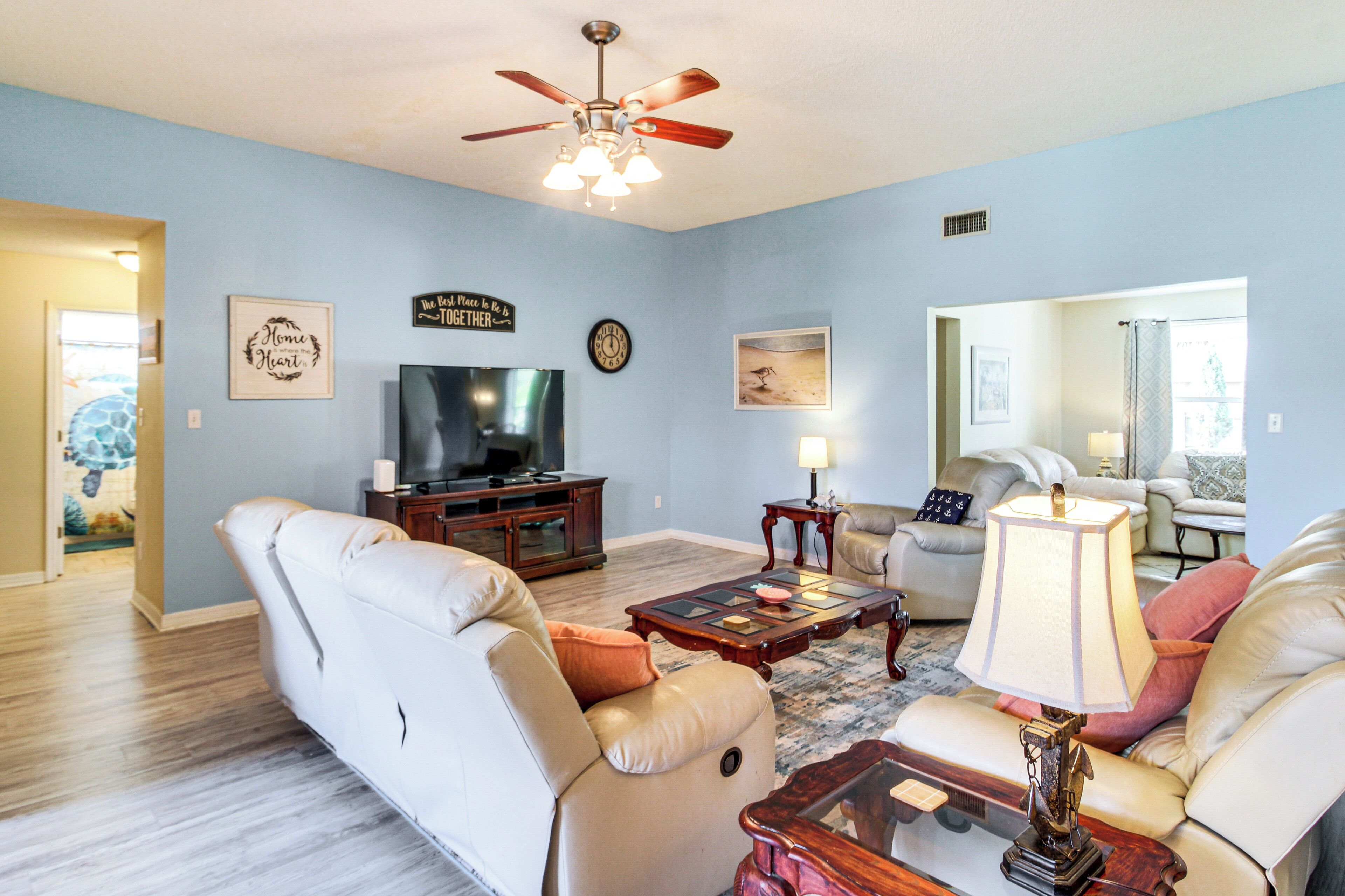 A living room with a beige sofa, a coffee table, a TV, and a ceiling fan.