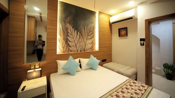 A modern hotel room with a large bed, a mirror, a wall-mounted artwork, a bedside table with a lamp, and a small potted plant. - Staykart Boutique Hotel  (Bhilwara)