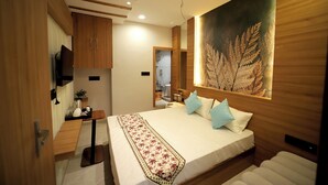 A modern bedroom with a large bed, wooden headboard, a painting, and a small table with a plant. - Staykart Boutique Hotel  (Bhilwara)