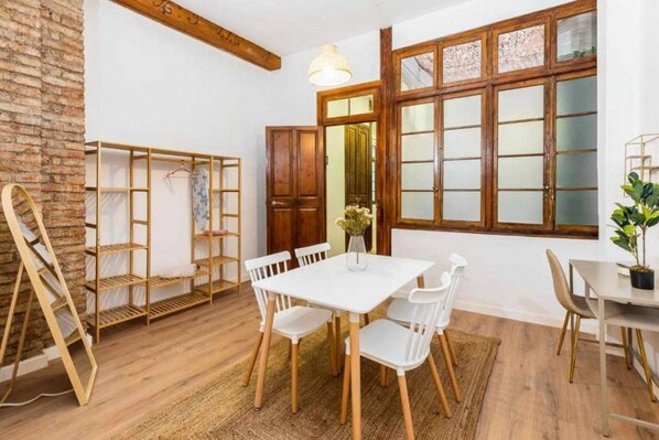 Ein Essbereich mit einem weißen Tisch und Stühlen, Holzregalen und einem großen Fenster mit Milchglas.