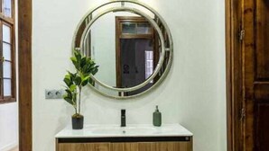 A bathroom with a wooden vanity, a round mirror, and a potted plant.