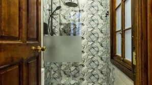 A narrow bathroom with a shower, wooden doors, and a patterned wall.