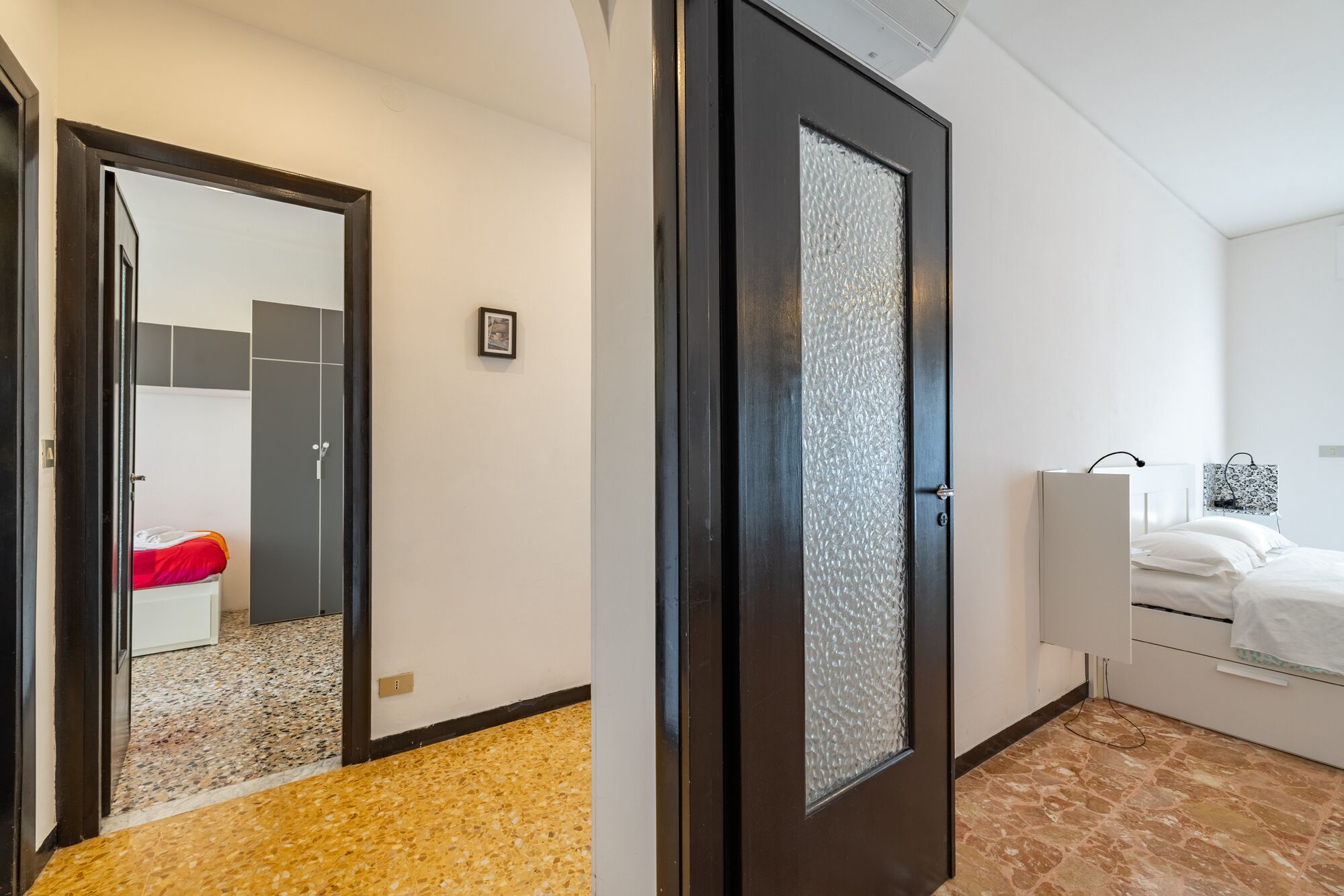 A hotel room with a bed, a bedside table, a wardrobe, and a door with frosted glass.