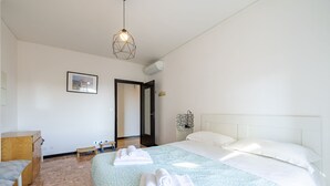 A hotel room with a bed, a desk, a chair, a hanging light fixture, and a framed picture on the wall.