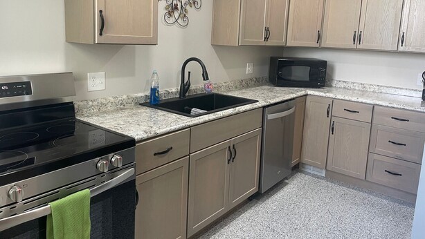 Una cucina con mobili color beige, un piano di lavoro in granito, un lavello nero, un fornello in acciaio inossidabile e un forno a microonde.
