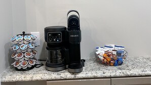 Un piano di lavoro in cucina con una macchina per il caffè, una Keurig, un portapodi di caffè e un cestino pieno di capsule.