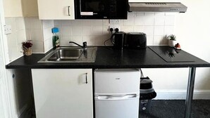 Una cocina compacta con armarios blancos, una encimera negra, microondas, cafetera y un refrigerador pequeño.
