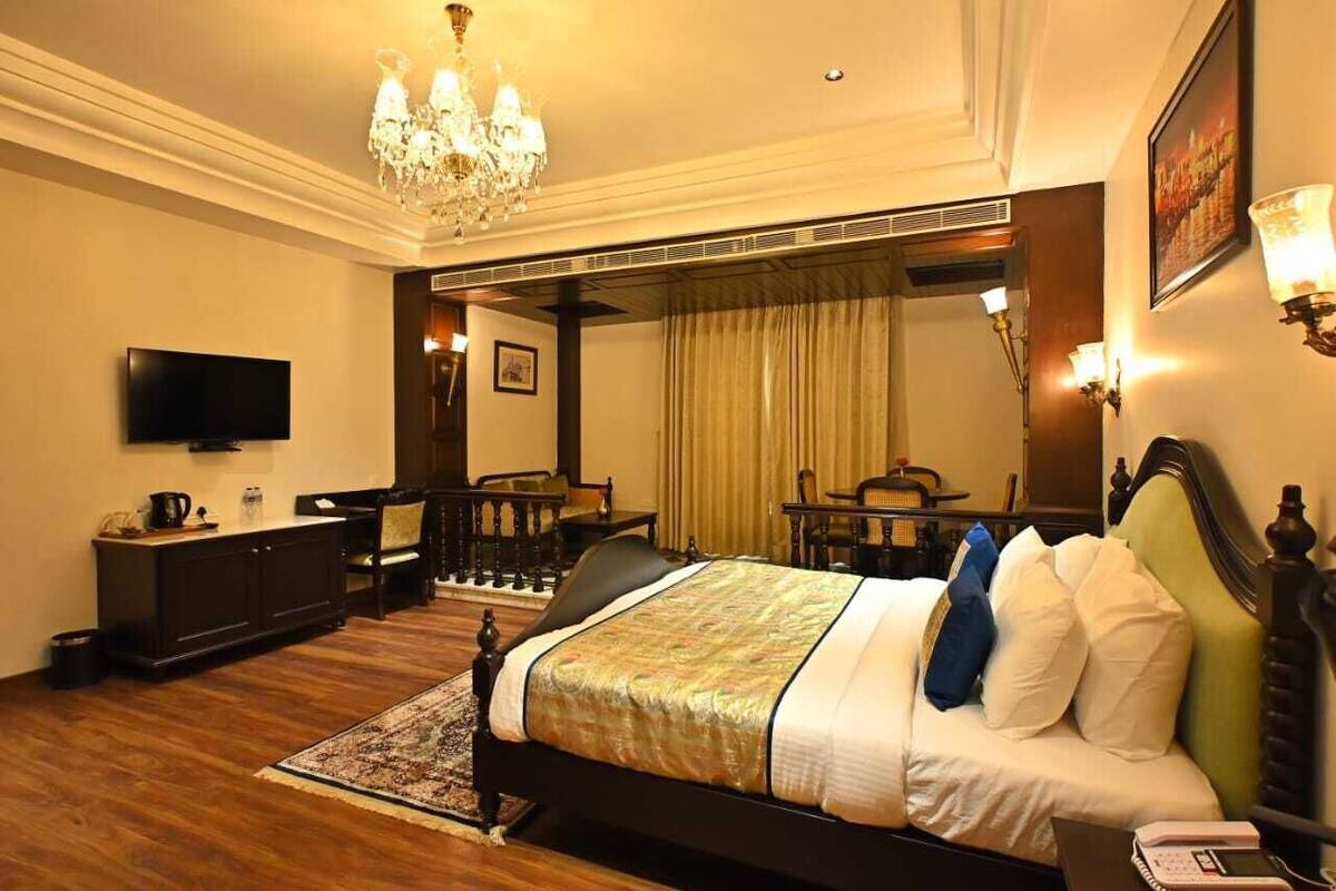 A hotel room with a large bed, a television, a desk, and a chandelier.