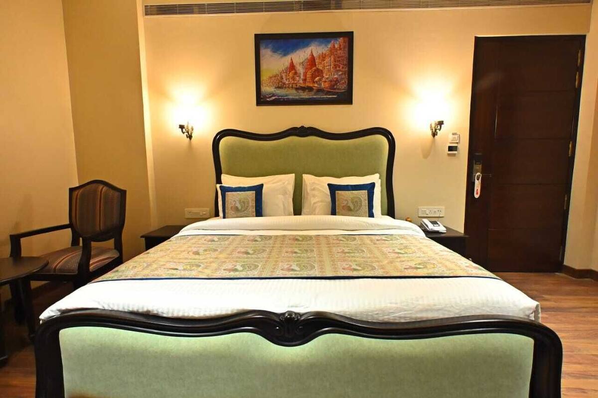 A hotel room with a bed, a chair, a nightstand, a painting on the wall, and a door.