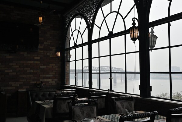 A restaurant with brick walls, large windows, and a view of a bridge over water.