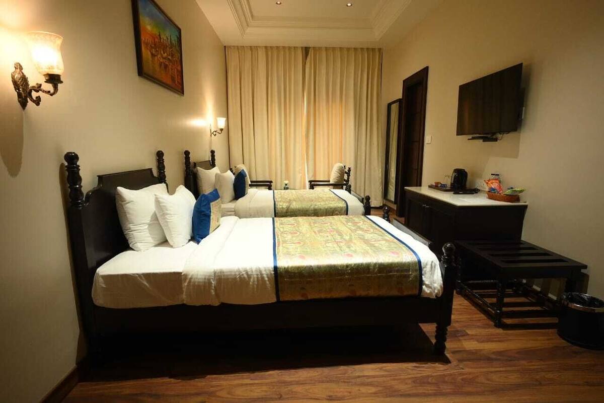 A hotel room with two beds, a desk, a television, and a painting on the wall.