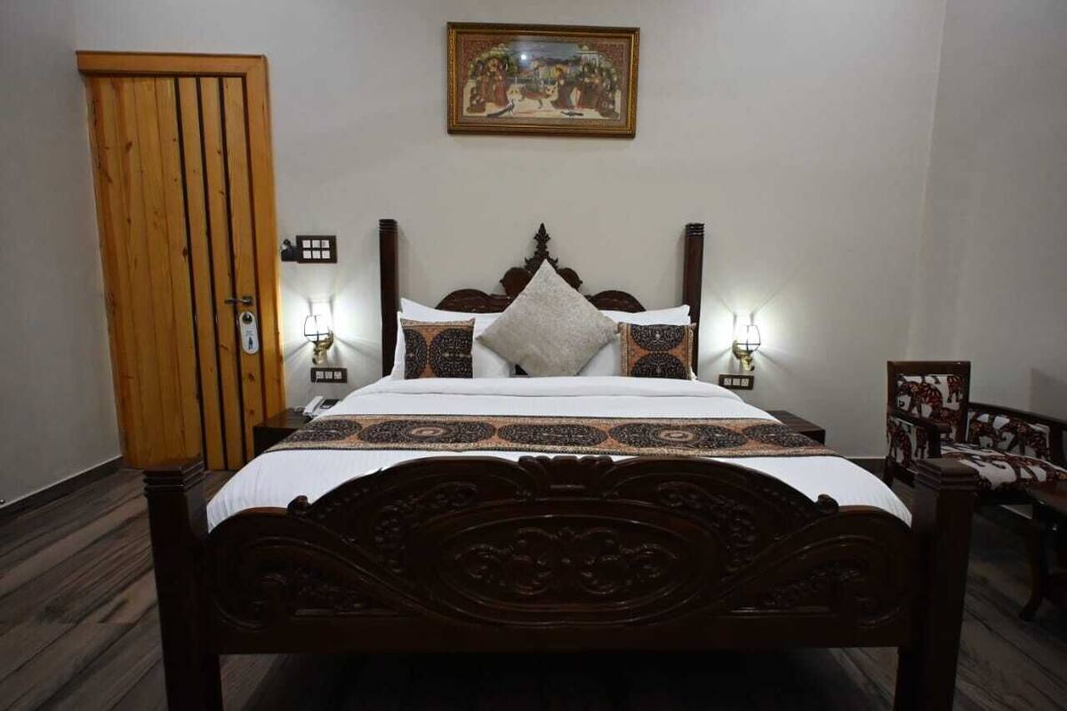 A wooden bed with a headboard, two bedside tables with lamps, a wooden wardrobe, and a framed picture on the wall.