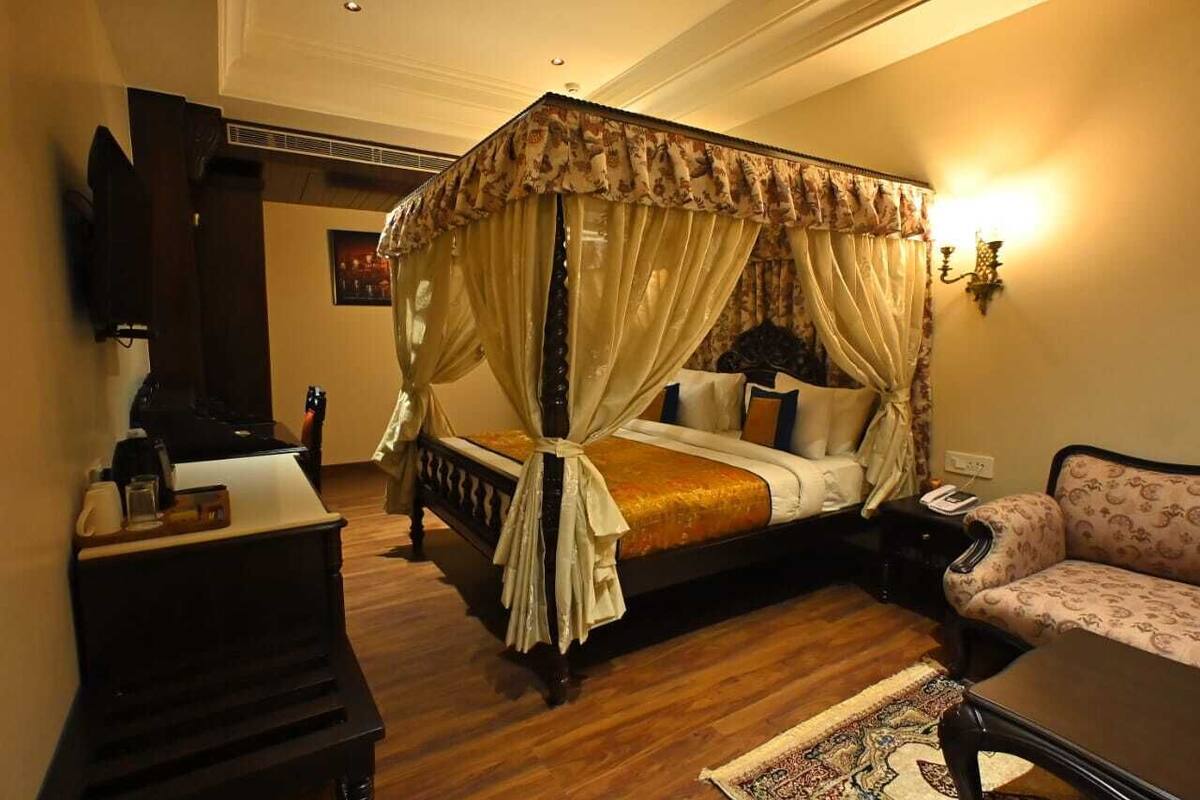 A four-poster bed with a canopy, a sofa, a desk, and a television in a hotel room.
