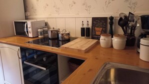 A compact kitchen with a microwave, stove, and wooden countertop. There are jars, a cutting board, and kitchen utensils on the counter.