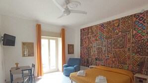 Una habitación de hotel con cama, escritorio, silla, sofá azul y ventilador de techo, además de una pared con diseño.