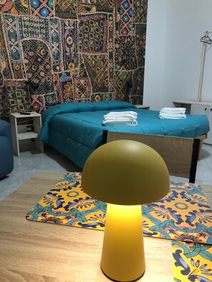 A room with a bed, a bedside table, a tapestry, and a lamp.