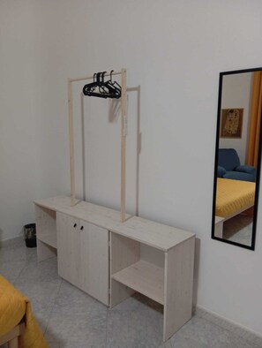 A room with a wooden desk, a hanging rack, and a bed with a yellow bedspread.