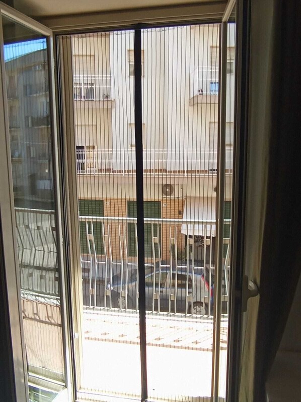 A view through a window with vertical blinds, revealing a building with multiple floors and balconies.