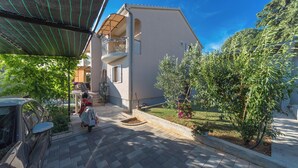 A residential building with a balcony, a paved courtyard, and a garden area. - Apartments Jukic (Sveti Filip i Jakov)