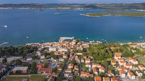 An aerial view of a coastal town with a marina, buildings with red-tiled roofs, and a clear blue sea.