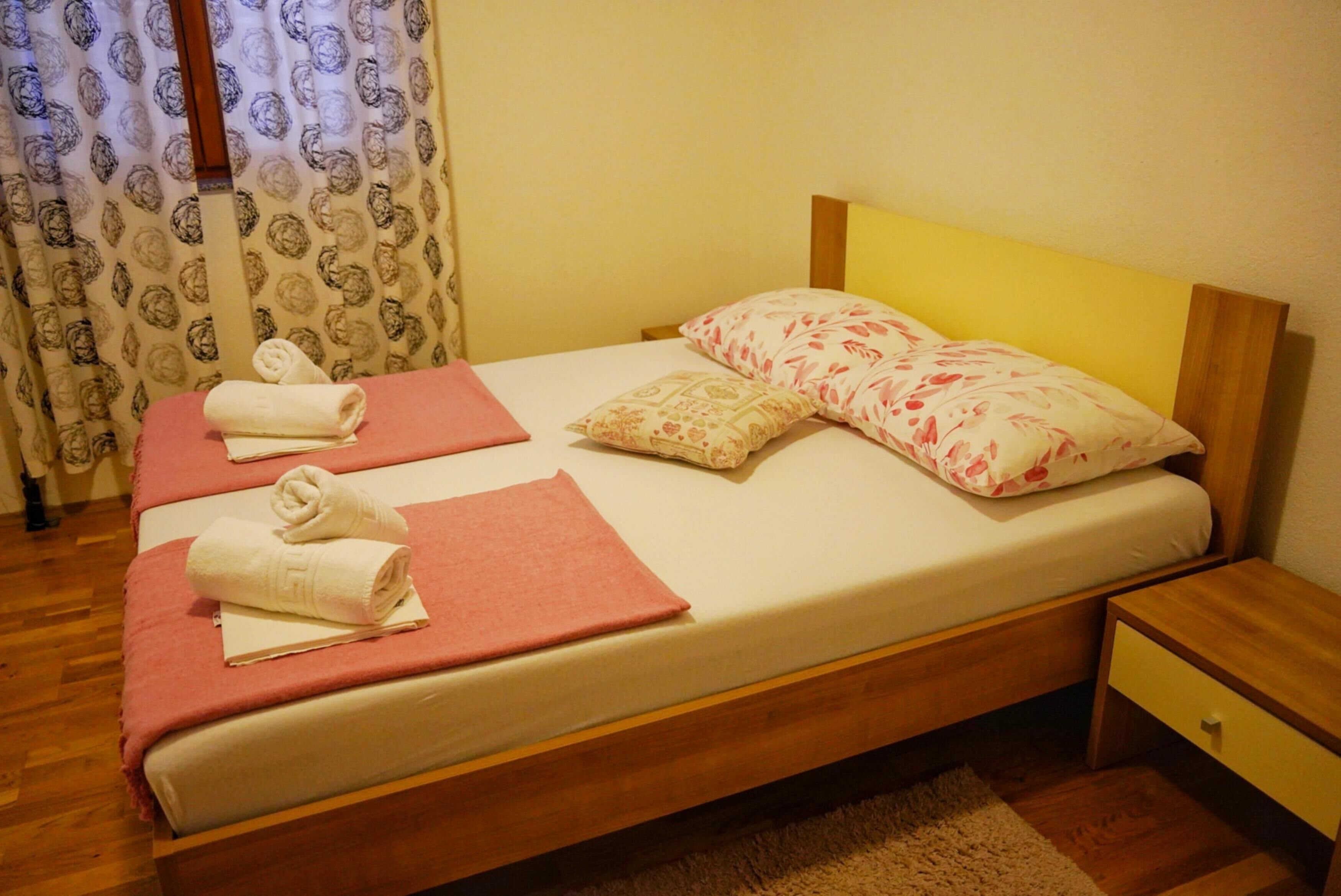 A neatly made bed with two pillows, a folded towel, and a pink blanket.