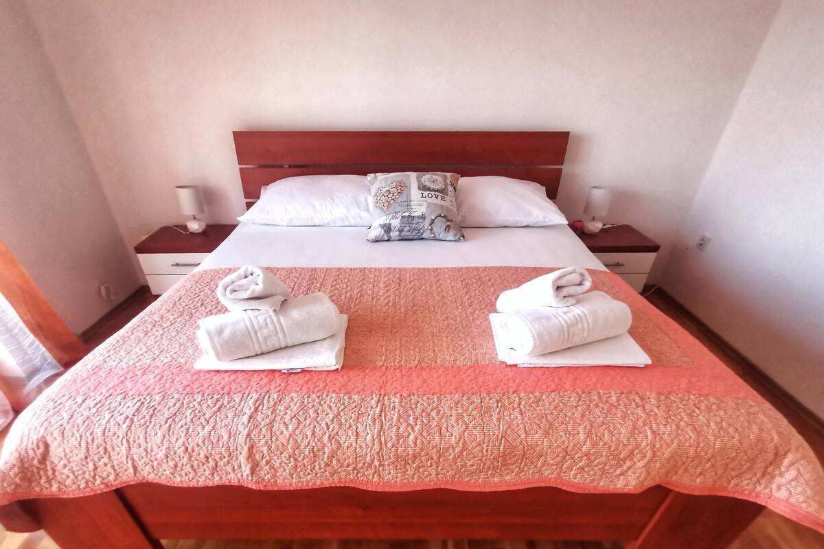 A neatly made bed with a red bedspread and two towels folded on the bed.
