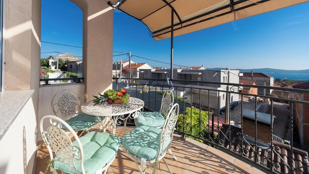 A balcony with a table, chairs, and a view of the cityscape. - Apartments Jukic (Sveti Filip i Jakov)