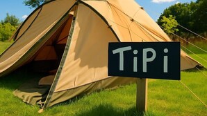 Een tent met een bordje met de tekst 'Tipi' in een grasveld.