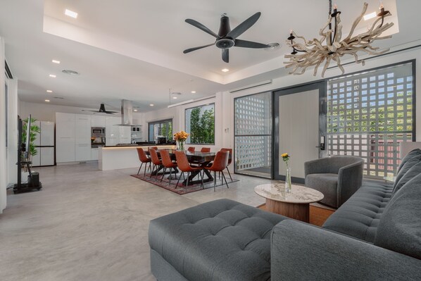 Ein modernes Wohnzimmer mit grauem Sofa, einem Essbereich mit Tisch und Stühlen, einer Küche im Hintergrund und einer großen Schiebeglas-Zuwegung zum Balkon.