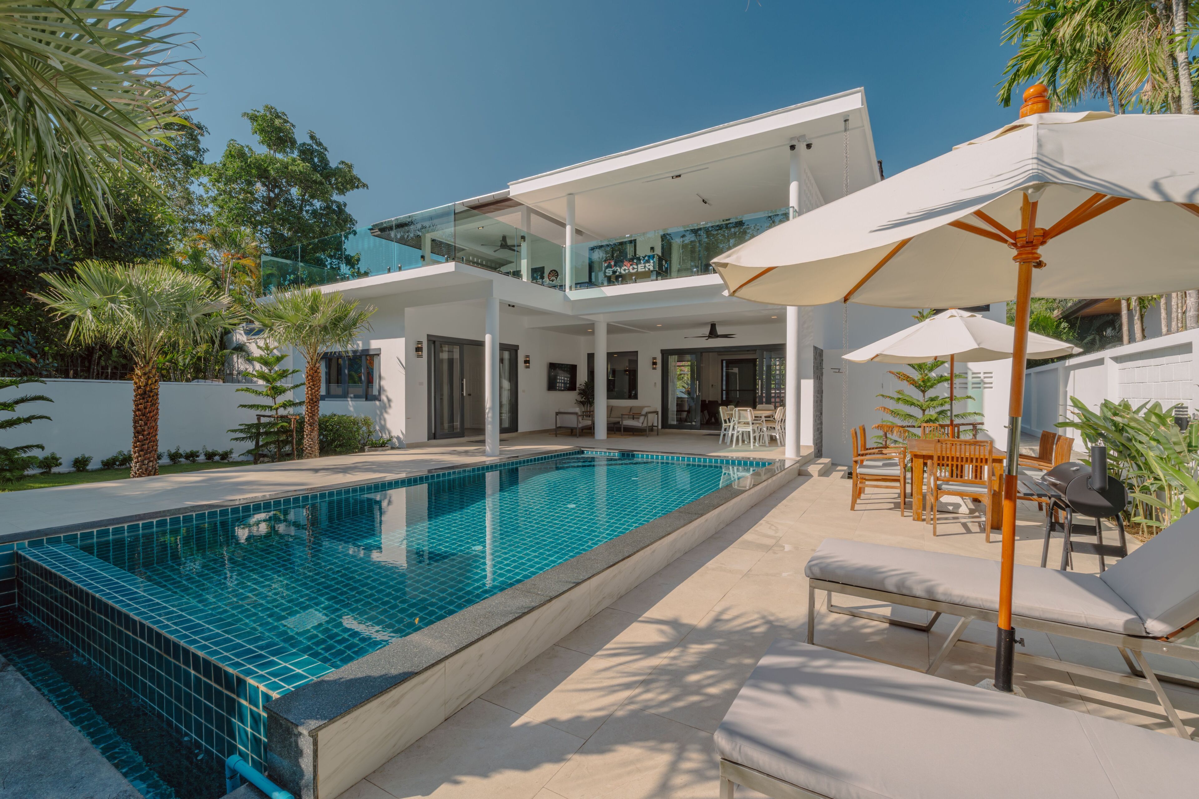 Ein modernes, zweistöckiges Haus mit Swimmingpool, Gartenmöbeln und Palmen.