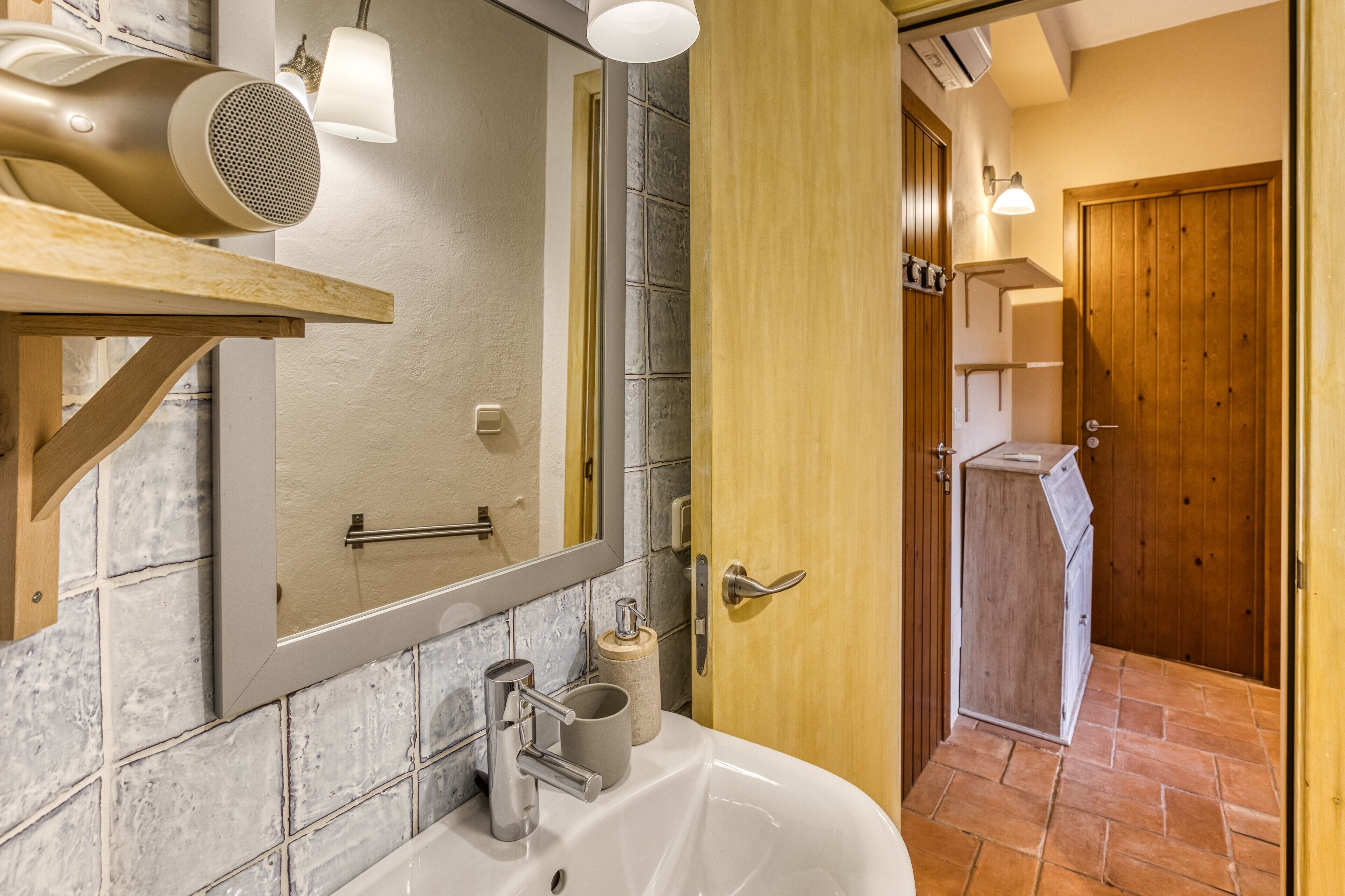 A bathroom with a white sink, a mirror, a hairdryer, and a wooden door.