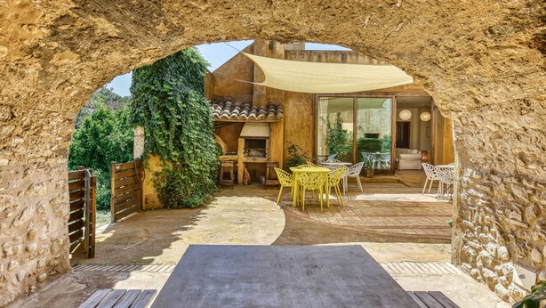 An outdoor patio with stone walls, a wooden table, yellow chairs, and a covered seating area. - Room 'Sajolida' with Shared Pool, Wi-Fi and Air Conditioning (Borrassà)