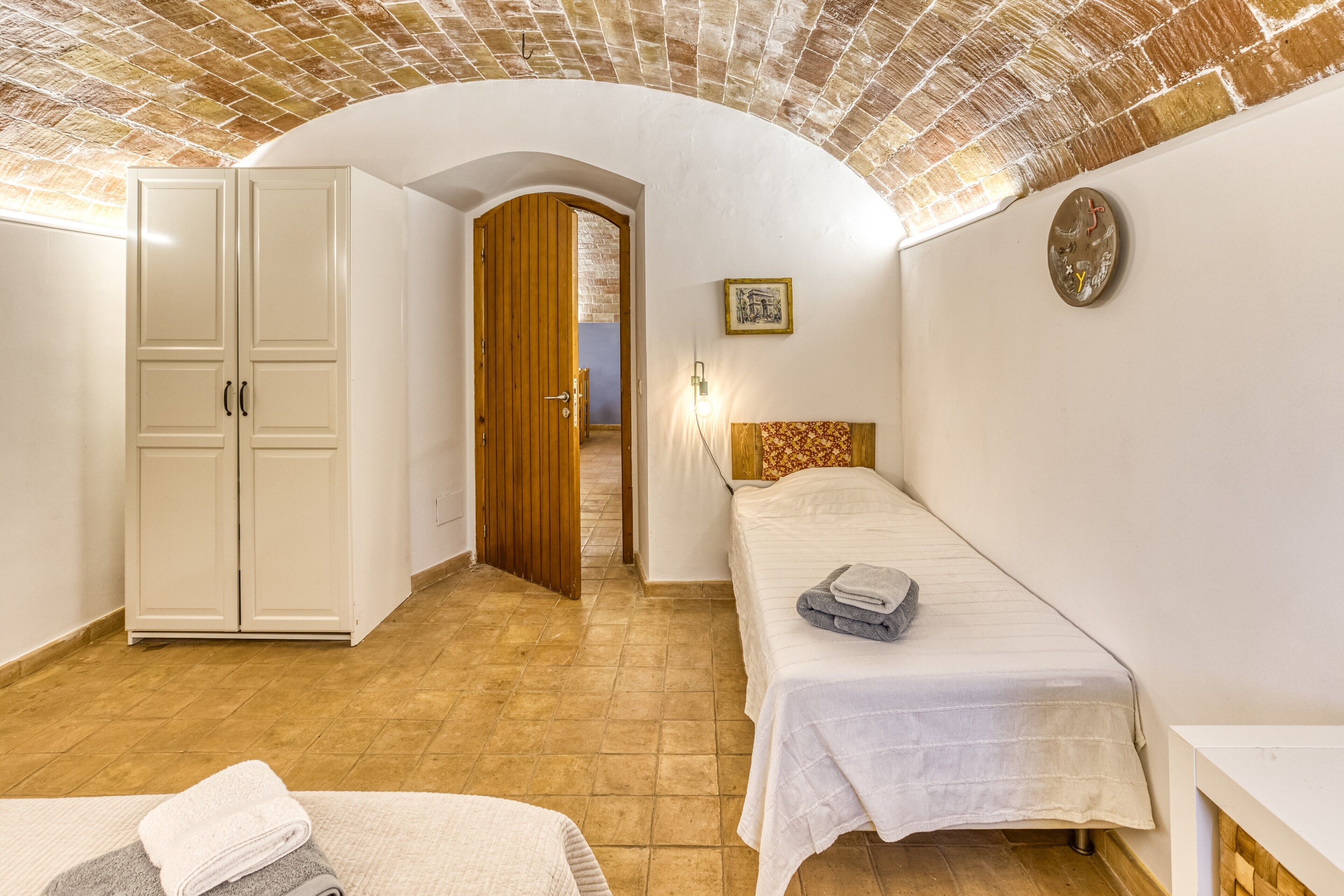 Une chambre à coucher comprenant un lit, une armoire, une porte donnant sur une autre pièce et un luminaire fixé au mur.