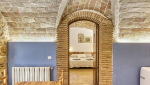 Une pièce avec un mur en pierre, une table en bois, un radiateur et un lit avec des oreillers et une couverture.