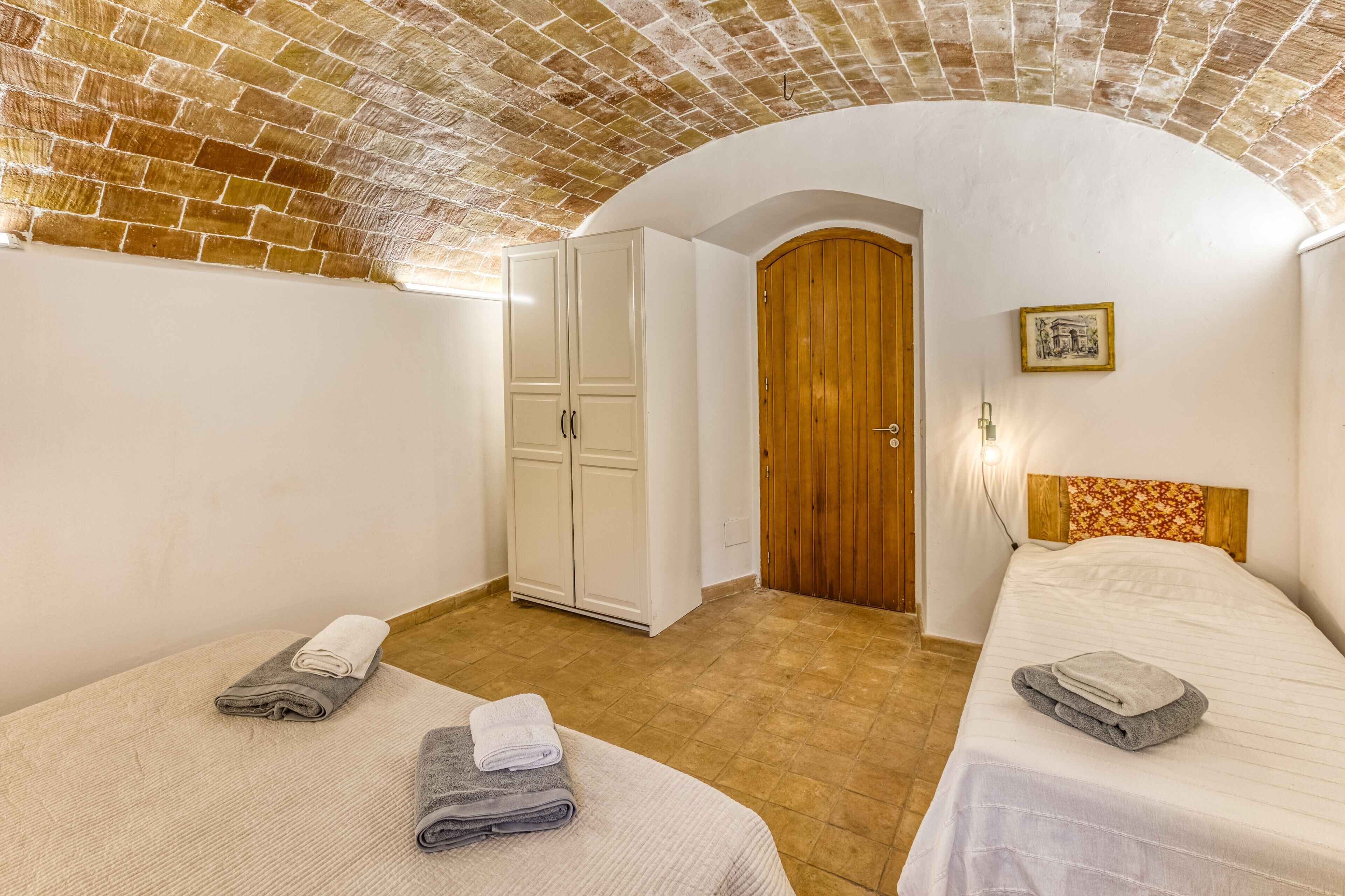 Una habitación con dos camas, una puerta de madera, un armario blanco y un techo de ladrillo.