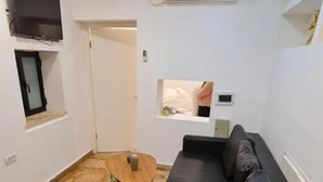 A compact living space with a black sofa, a small round table, and a TV mounted on the wall. - SpaceART (Jerusalem)