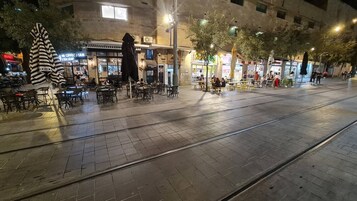 Una plaza urbana nocturna con terrazas en cafés, una vía de tranvía y diversos comercios y restaurantes.