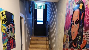 A hallway with a checkered floor, a staircase leading to a door with Hebrew text, and colorful graffiti art on the walls. - SpaceART (Jerusalem)
