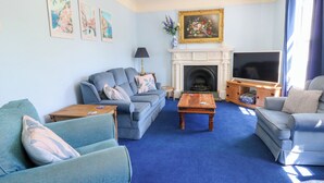 Ein Wohnzimmer mit blauem Sofa, blauem Sessel, Couchtisch aus Holz, Kamin und Fernseher.
